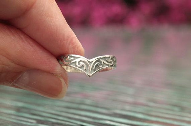 Silver ring with intricate design held by a hand against a blurred background