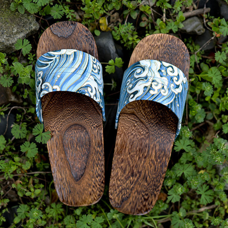 Wooden sandals with blue and white wave design on a green leafy background