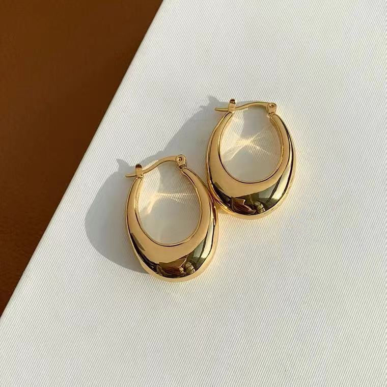 Gold hoop earrings with a white stone on a light background