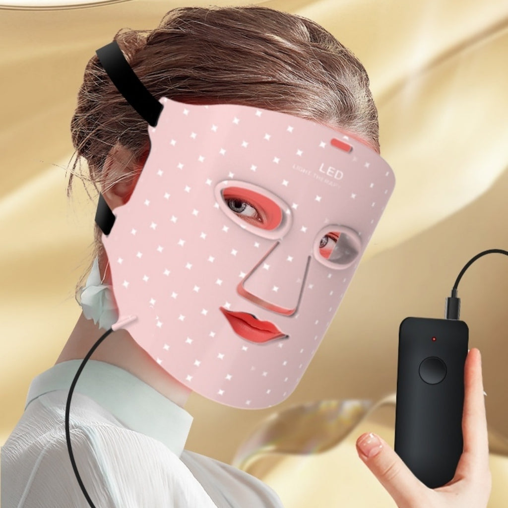 Woman wearing a pink LED face mask with a remote control on a gold background