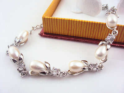 Pearl bracelet with silver accents on a white surface with a wooden box in the background