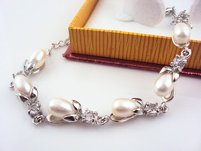 Pearl bracelet with silver accents on a white surface with a jewelry box in the background.