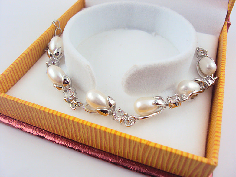 Pearl bracelet with silver accents on a white stand inside an open jewelry box.