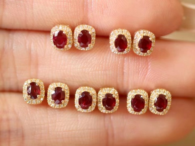 Gold earrings with red gemstones on a hand