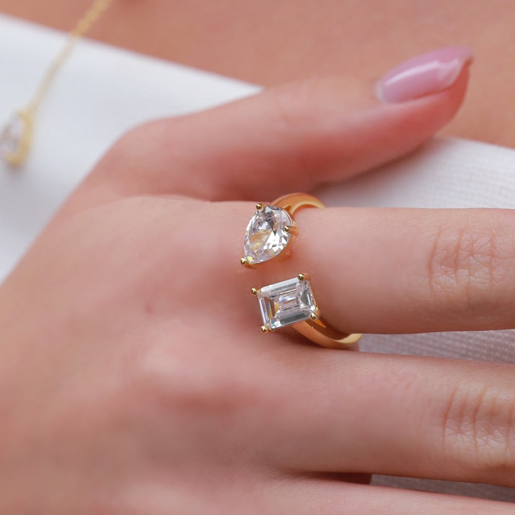 Gold rings with clear gemstones on a hand against a neutral background
