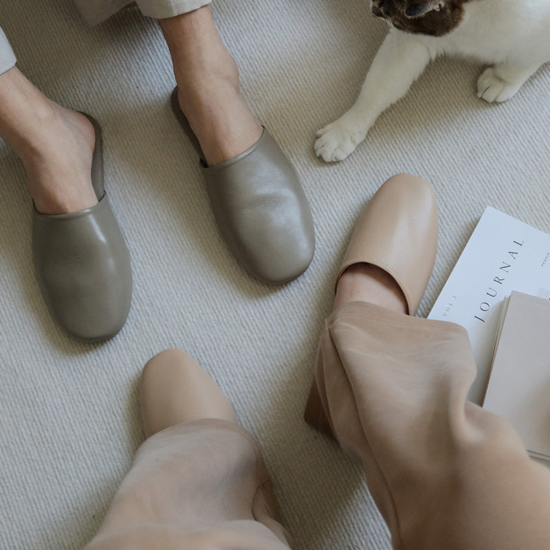 Two pairs of feet wearing flat shoes on a light-colored floor with a cat and book in the background.