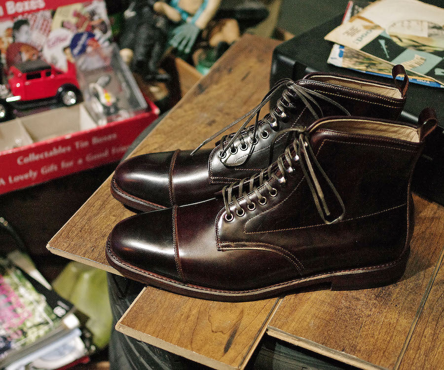 Pair of brown leather boots on a wooden surface with a cluttered background
