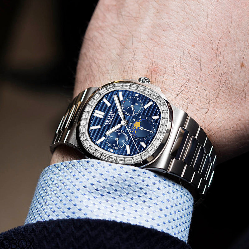 Luxury watch with a blue face on a person's wrist, wearing a light blue shirt.
