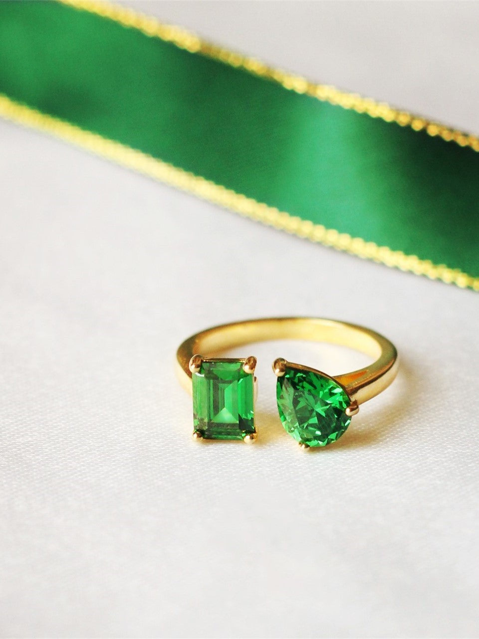 Gold ring with green gemstones on a white background