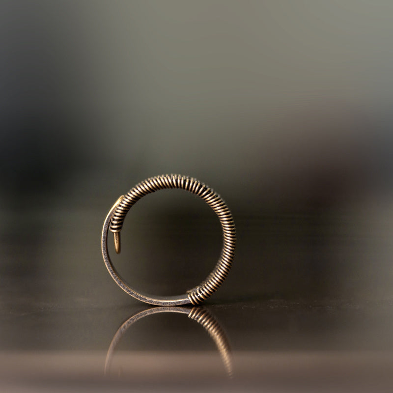 Bronze hoop earring on a reflective surface with a dark background
