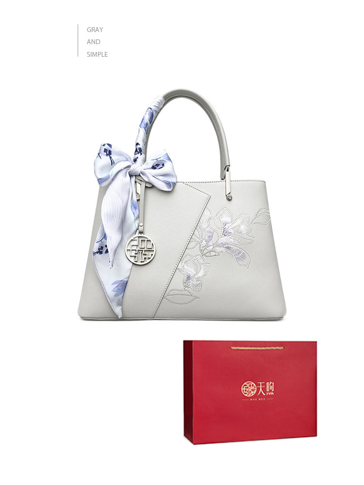 Gray handbag with floral ribbon and red gift box on a white background