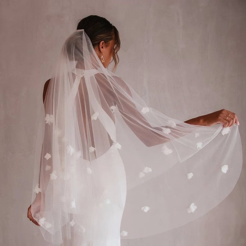 Woman holding a sheer white veil with small polka dots against a plain background