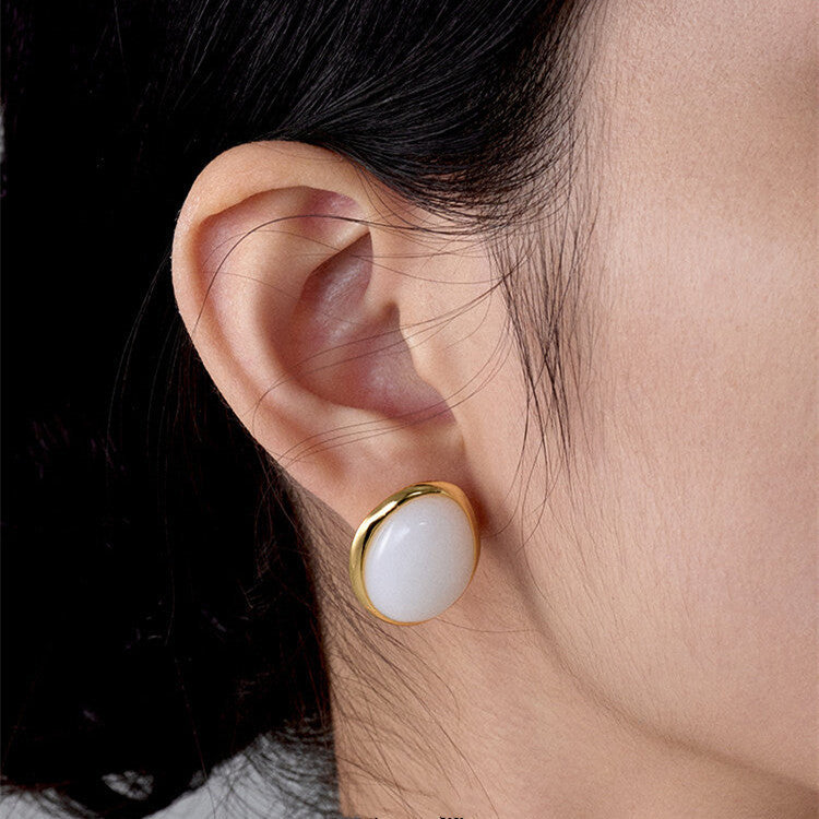 Close-up of an ear wearing a gold and white earring.