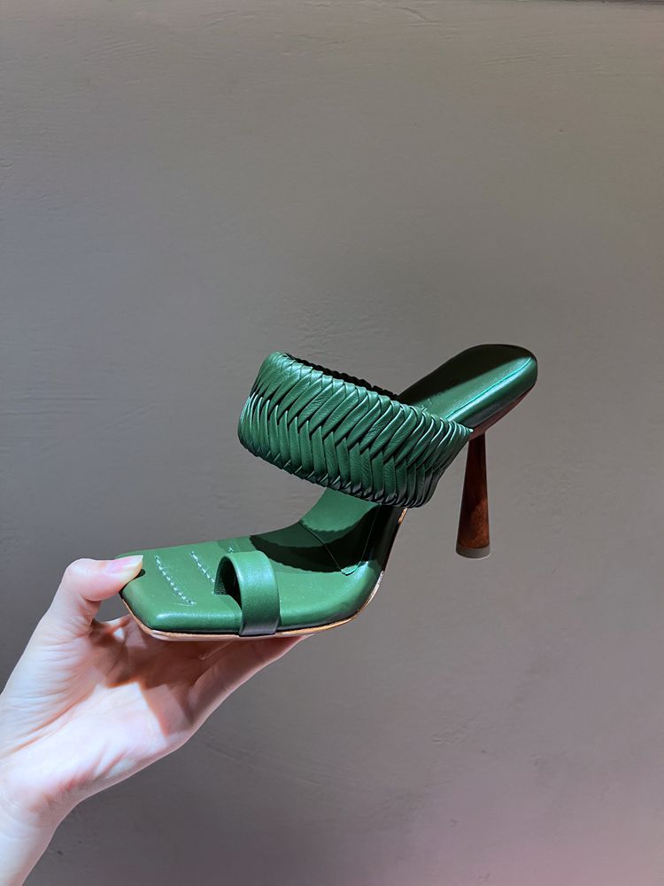 Green high-heeled shoe held by a hand against a plain background