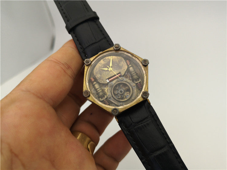 Hand holding a black wristwatch with a detailed face against a neutral background