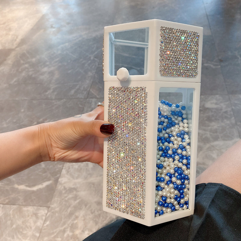 Hand holding a decorative box with rhinestone embellishments and pearls inside.