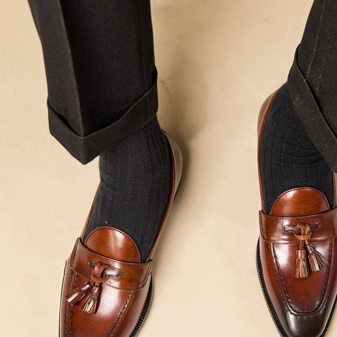 Brown loafers with tassels worn with black pants on a beige background