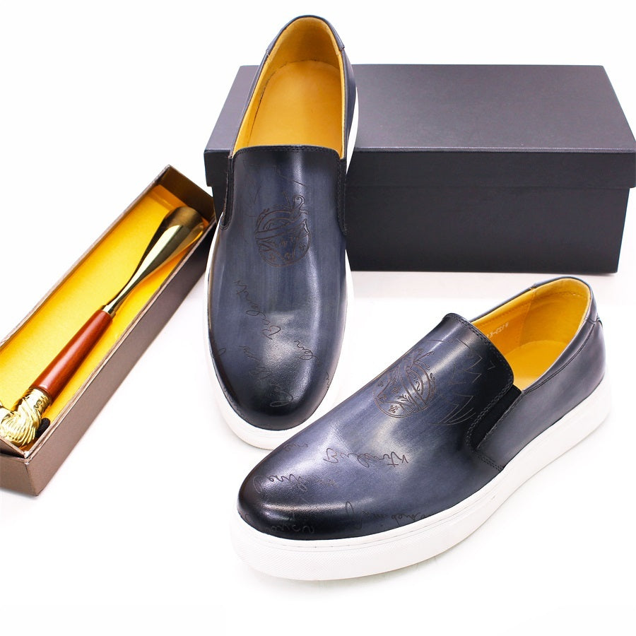 Pair of black loafers with white soles on a white background, next to a shoebox and shoehorn.