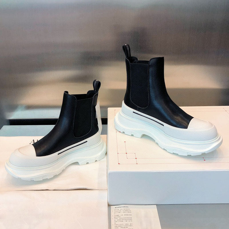 Black and white Chelsea boots on a white surface with a blurred background