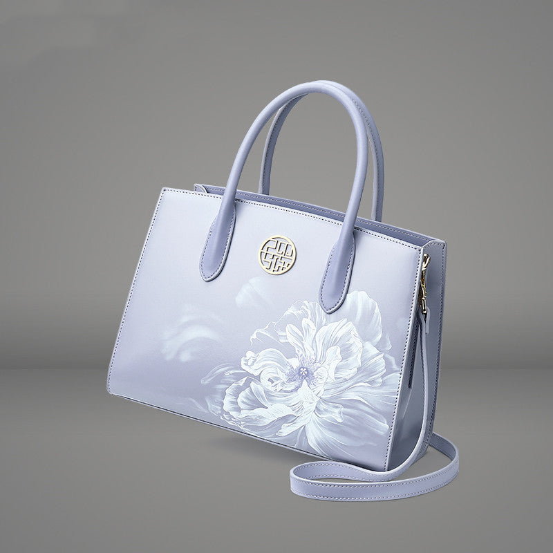 Light blue handbag with floral design and visible brand logo on a gray background