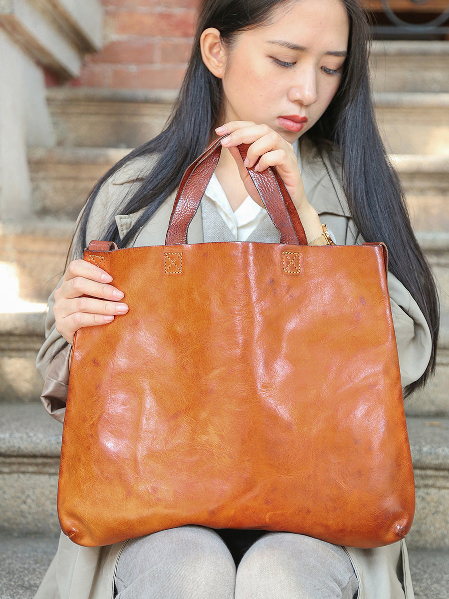 Woman holding a brown leather tote bag outdoors.