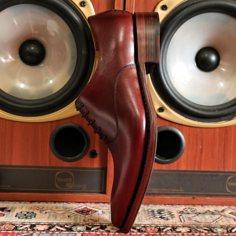 Brown leather dress shoe on a wooden speaker with 'Crown & Anchor' branding.