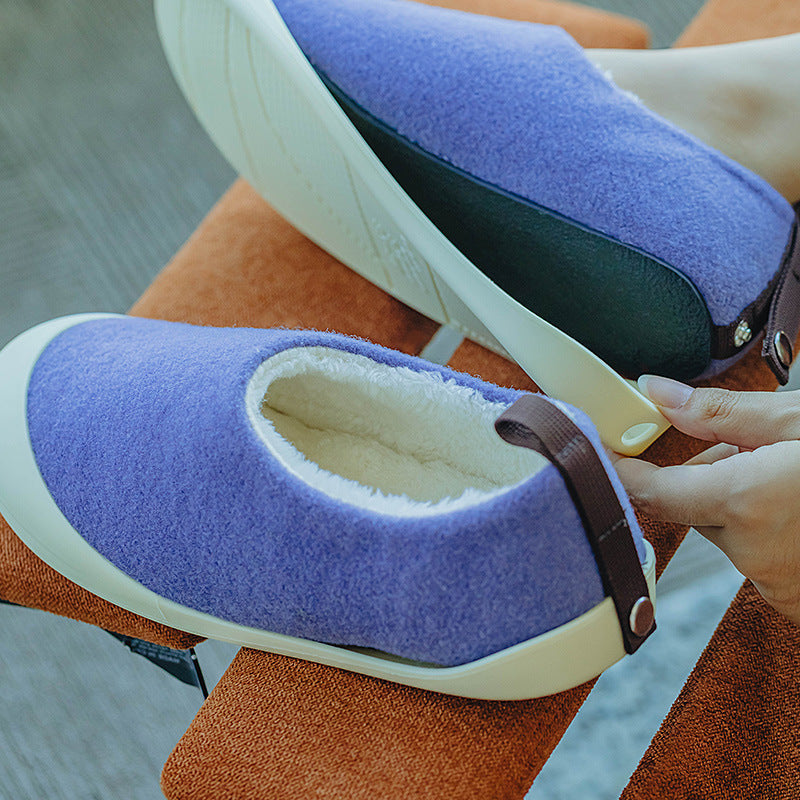 Purple slippers with white soles being worn by a person sitting on an orange cushion.