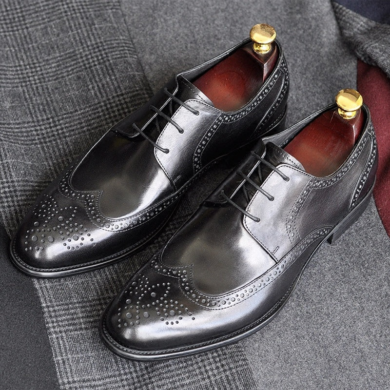 Pair of black leather dress shoes with gold buttons on a textured fabric background