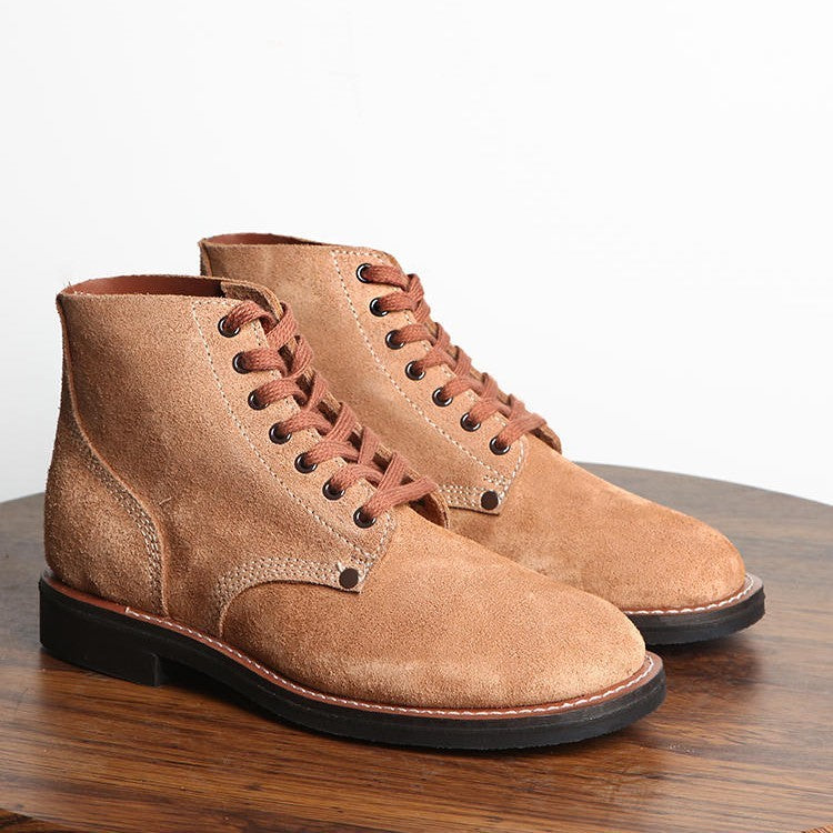 Pair of brown suede boots on a wooden surface with a white background