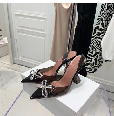 Black high-heeled shoes with decorative elements on a white box in a room setting.