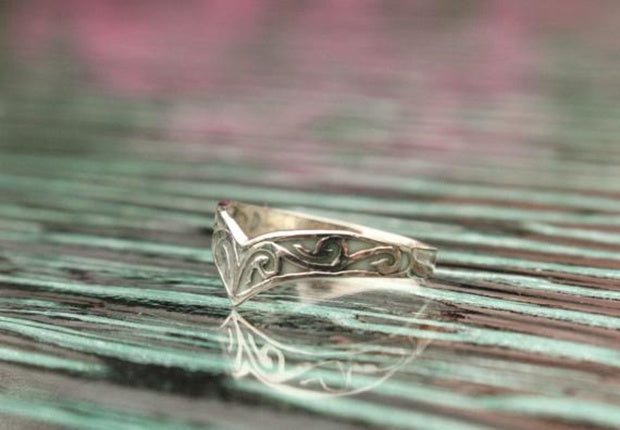 Silver ring with intricate design on a reflective surface