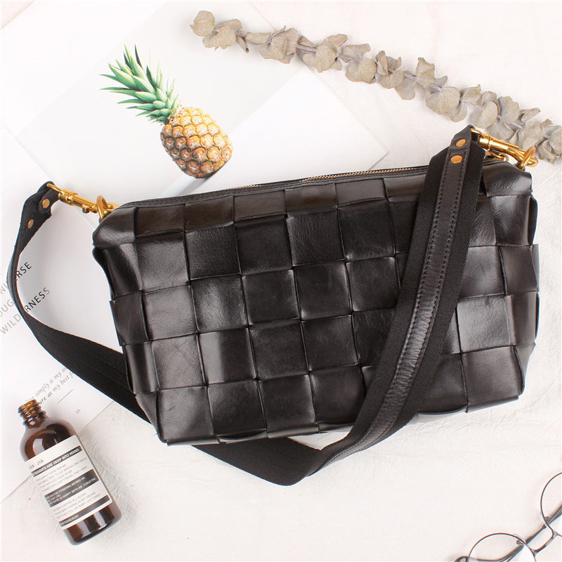 Black woven handbag on a white surface with a pineapple and bottle in the background