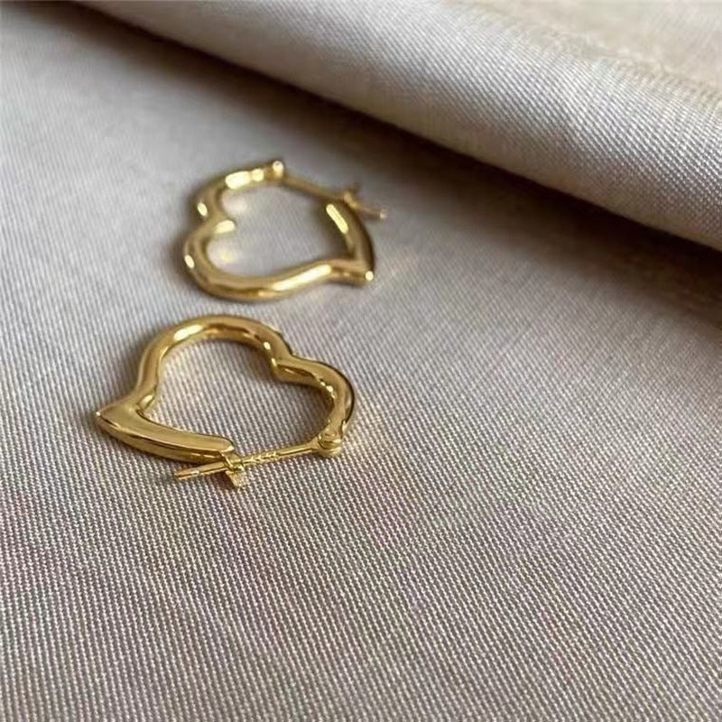 Gold heart-shaped hoop earrings on a beige fabric background