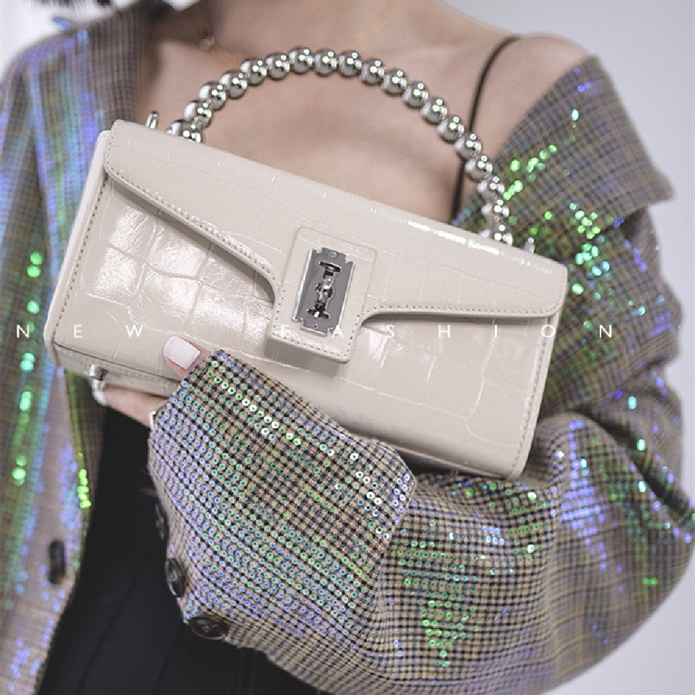 Beige handbag held by a person wearing a sequin jacket.