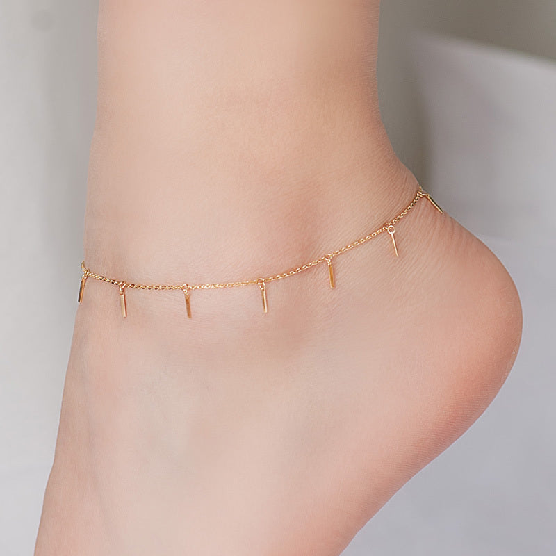 Gold anklet on a person's ankle against a neutral background