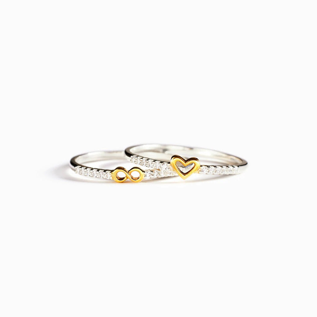Two gold and silver rings with heart and infinity symbols on a white background