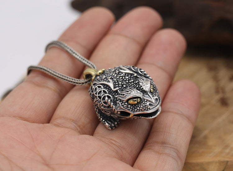 Silver frog pendant held in a hand with a blurred background