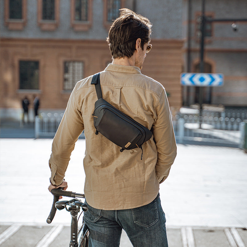 Man with a crossbody bag on a bicycle in an urban setting