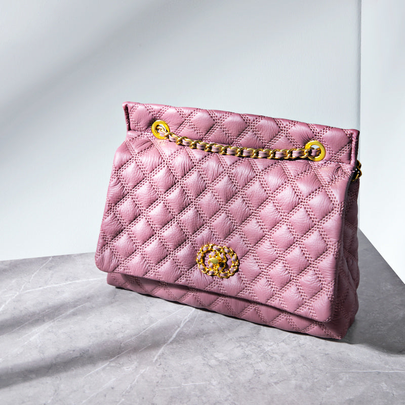 Pink quilted handbag with gold chain and clasp on a light gray surface.