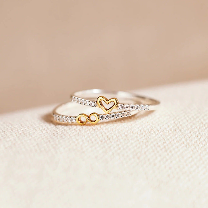 Two gold rings with heart and infinity symbol on a beige surface