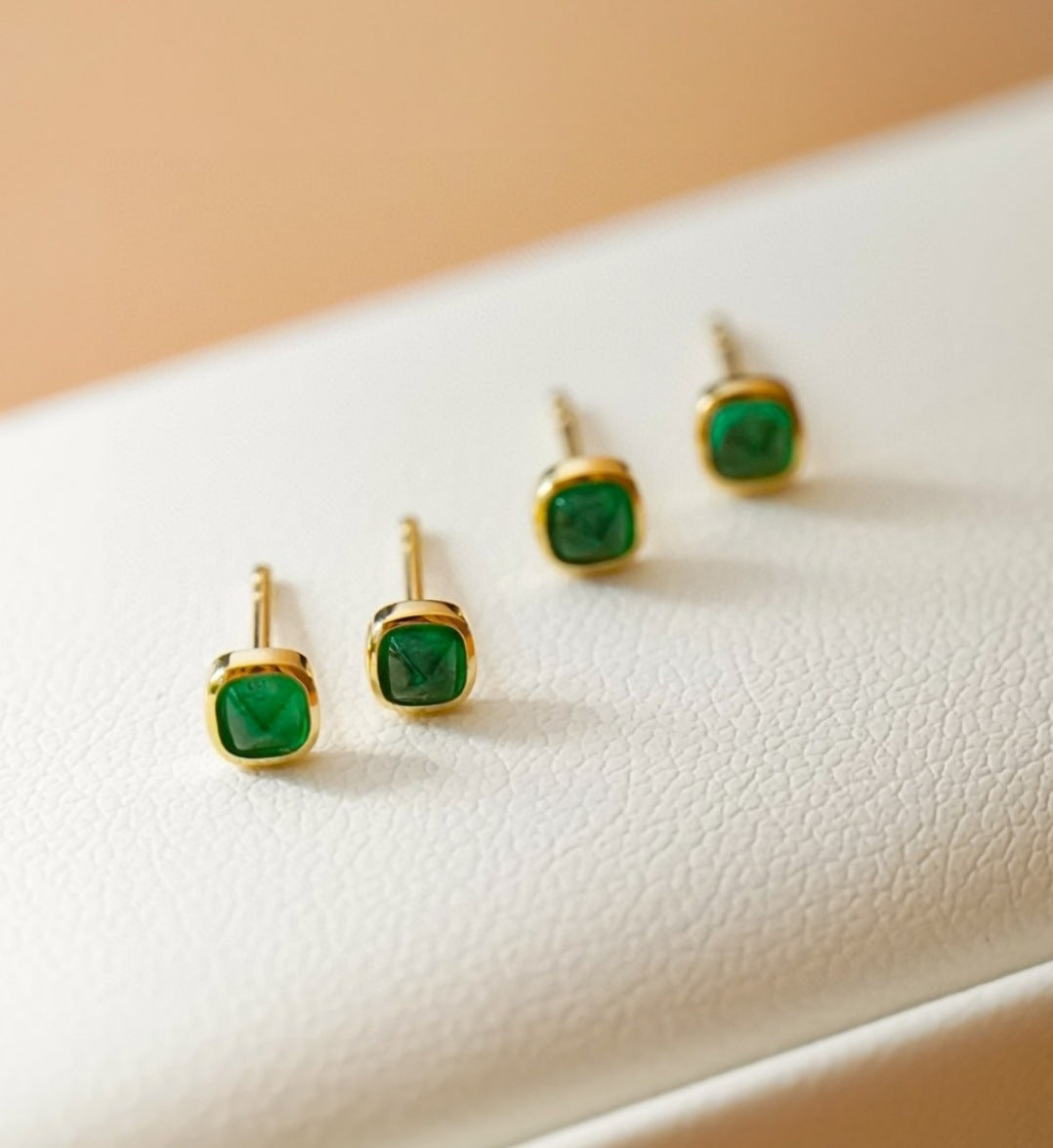 Gold earrings with green gemstones on a white surface