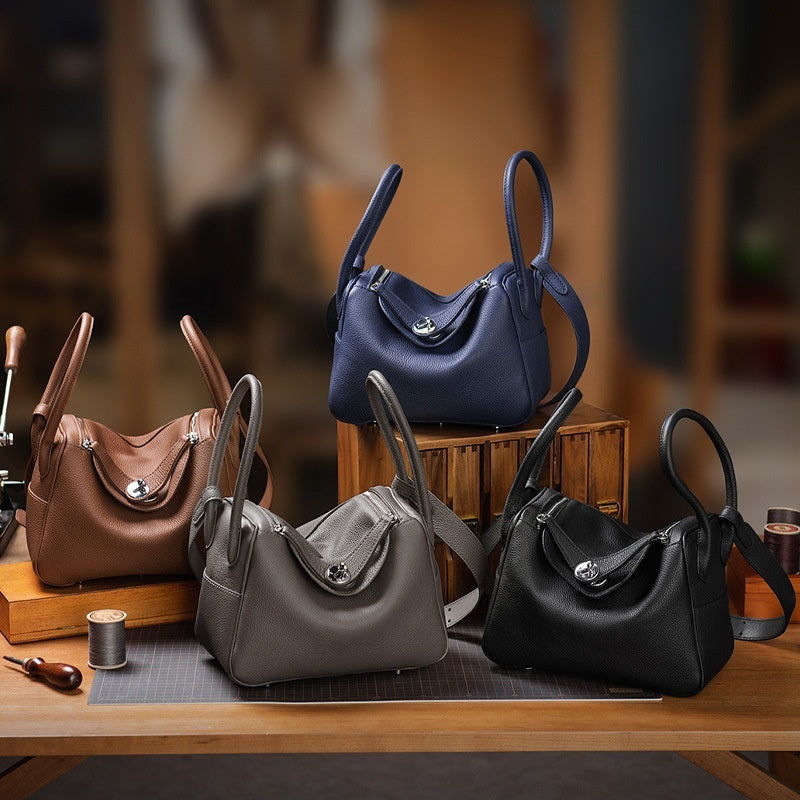 Four handbags in brown, blue, gray, and black on a wooden table with a blurred background.