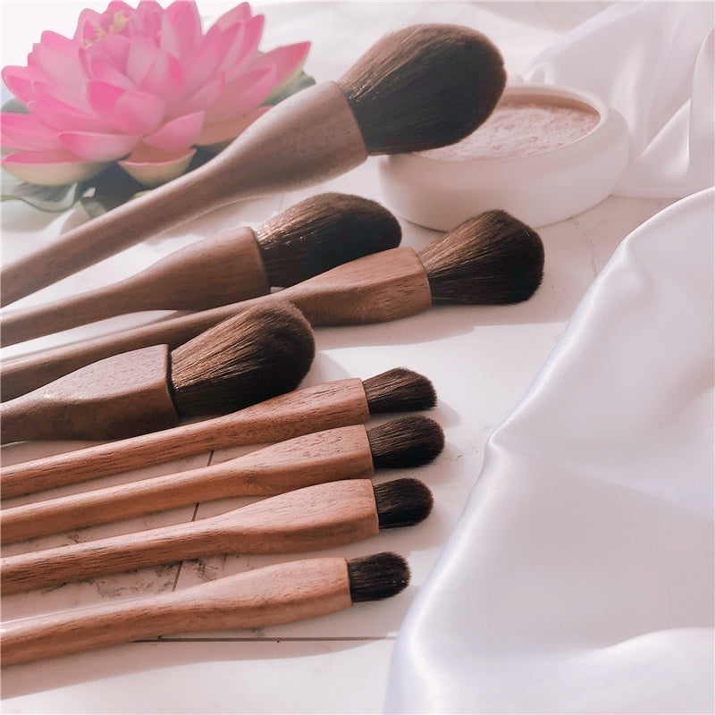Set of makeup brushes with wooden handles and black bristles on a light surface.