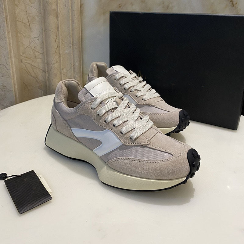 Pair of beige sneakers with white laces on a light surface.