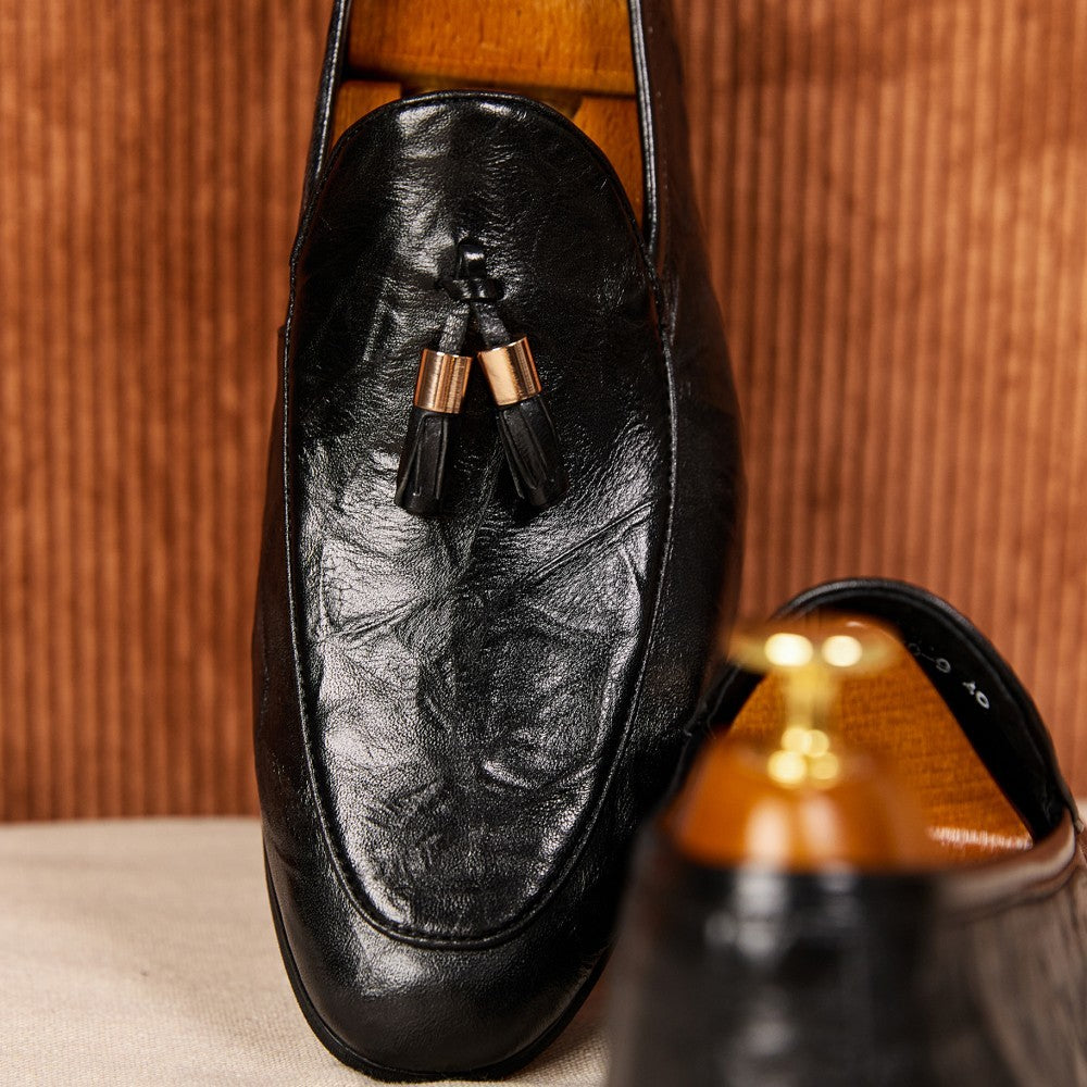 Black leather loafer with tassels on a wooden surface