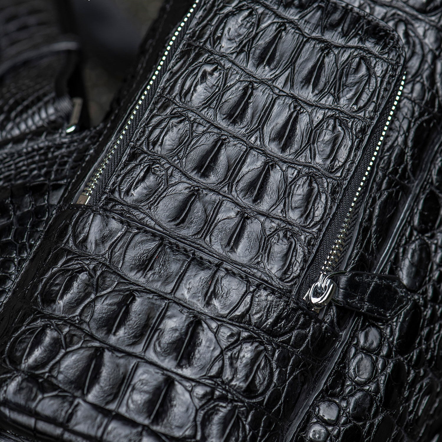 Close-up of a black crocodile skin bag with a zipper.