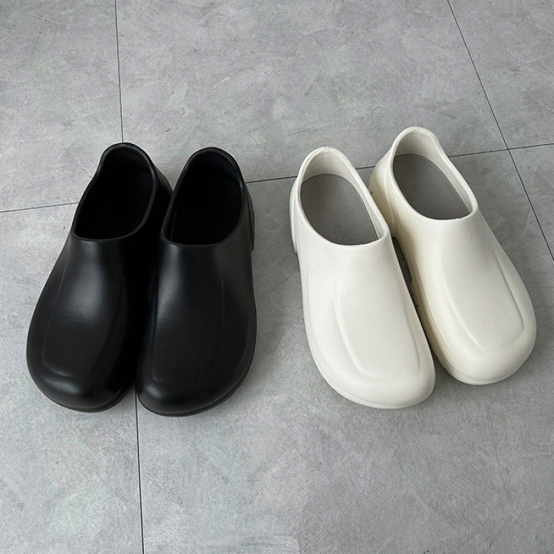 Pair of black and white slip-on shoes on a gray tiled floor.