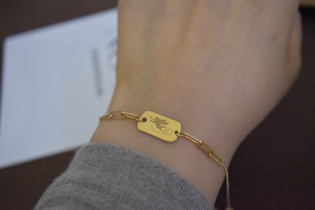 Gold bracelet with a tag on a wrist against a neutral background
