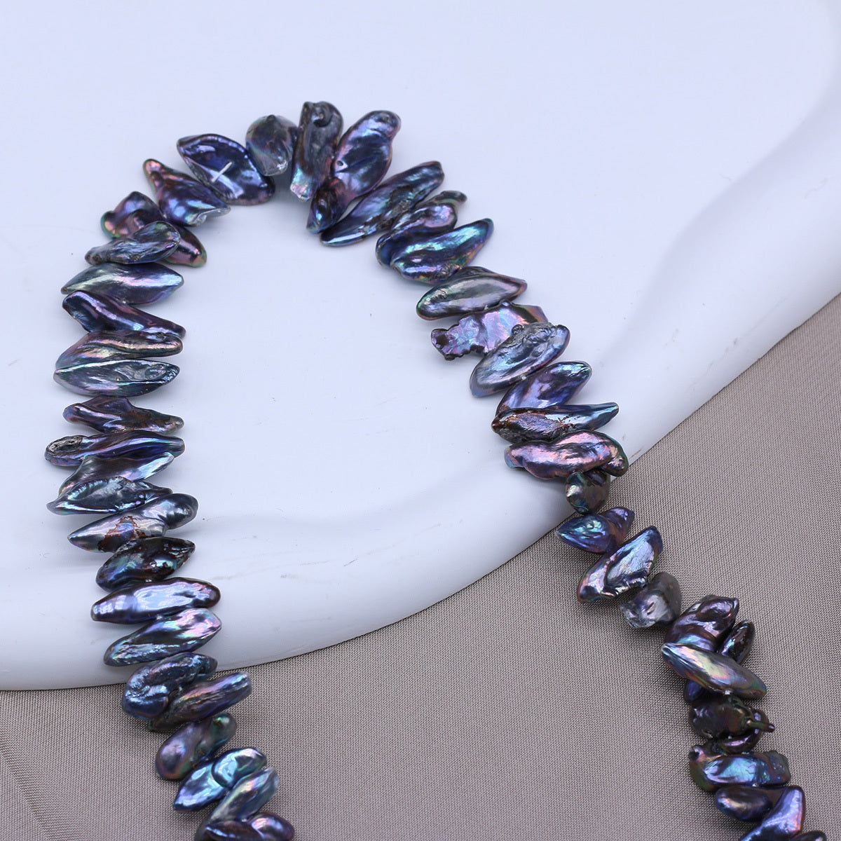 Necklace with dark, iridescent beads on a white and beige background