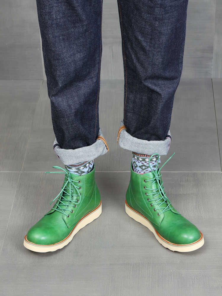 Green leather boots worn with dark jeans and patterned socks on a gray floor.